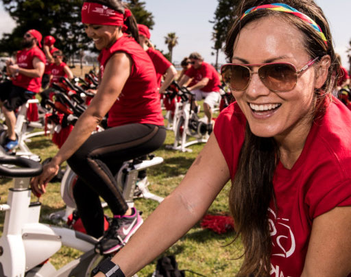 a group of people in red t-shirts riding stationary bikes in a park setting a group of people in red t-shirts riding stationary bikes in a park setting