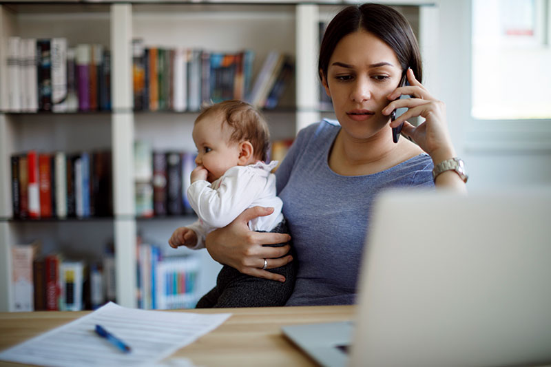 Busy working Mom on cell phone and laptop holding baby