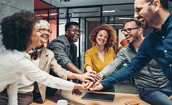 Smiling business persons stacking hands over the table